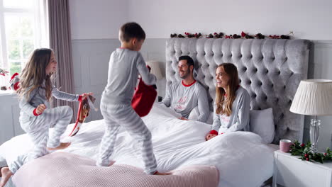 niños emocionados corriendo a la habitación de los padres en casa con medias y rebotando en la cama como familia regalos abiertos el día de navidad