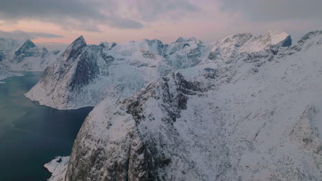 Orbiting-Lofoten-islands-frozen-extreme-terrain-and-icy-blue-ocean-aerial-view-at-sunset