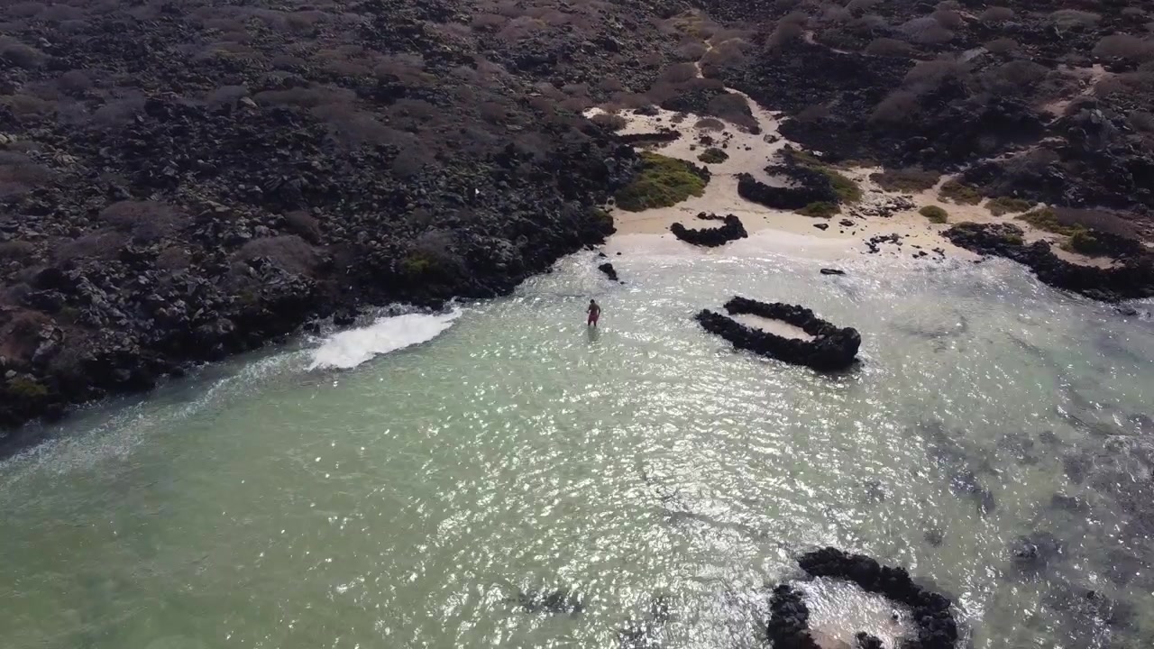 Riprese aeree con drone di un ragazzo che si rilassa su una bella spiaggia con acque turchesi a Lanzarote, Isole Canarie
