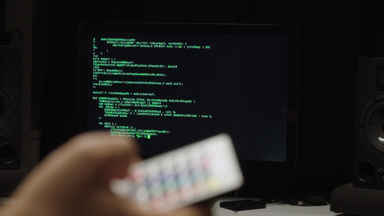 Shallow-focus shot of a hand using a remote control aimed at a monitor showing code—concept for AI control, automation, smart systems, remote management, and future technology interfaces