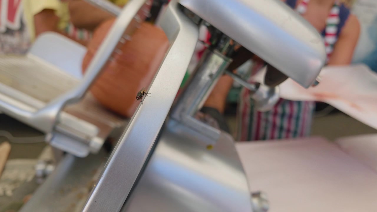 Close-up de uma lâmina de cortador de frios em movimento com frios fatiados por perto