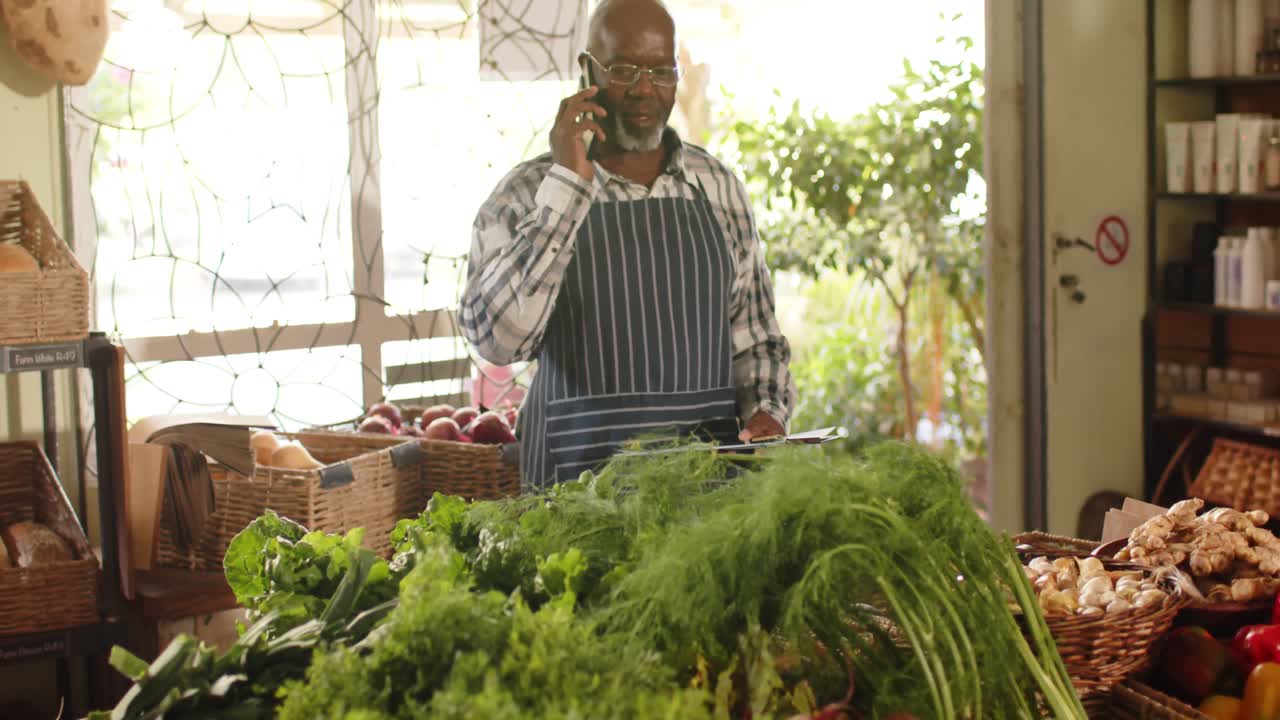 feliz anciano afroamericano dueño de una tienda hablando por teléfono inteligente en una tienda de alimentos saludables, cámara lenta