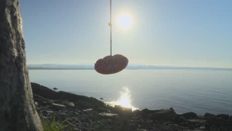 Seilschaukel-Bewegt-Sich-Sanft-Im-Wind-An-Der-Küste,-Während-Sich-Das-Frühmorgendliche-Herbstsonnenlicht-Vom-Meer-Reflektiert