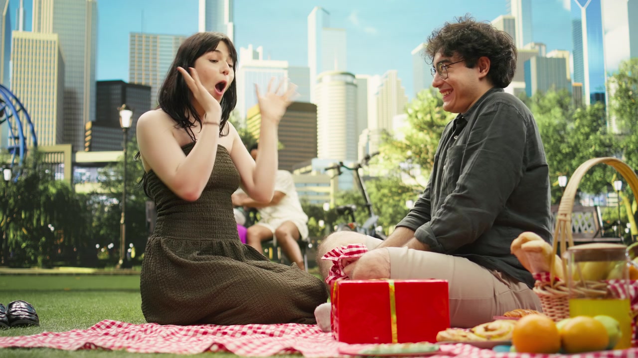Donna sorpresa che si copre la bocca mentre il partner sorridente rivela una scatola regalo rossa.