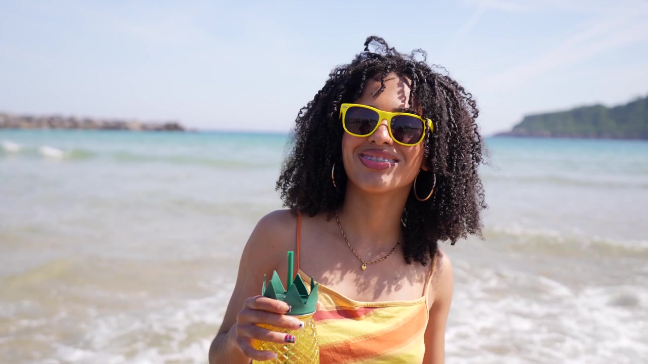 Mulher jovem sorridente com bebida de abacaxi em uma praia ensolarada