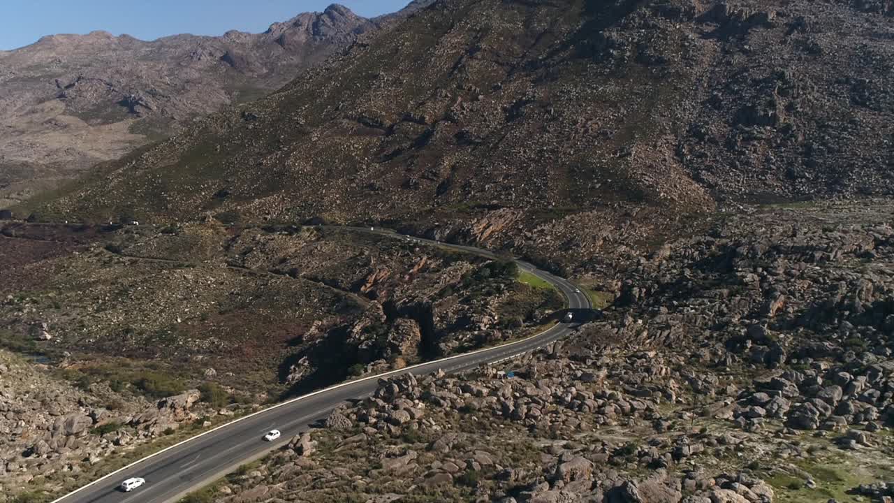 Veicoli ripresi dall'alto che percorrono un'autostrada su una ripida collina rocciosa frastagliata