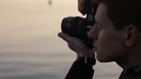 young caucasian photographer taking a picture with an analog camera at a lake sunset focus