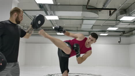 Slow-motion:-man-kicks-the-Boxing-paw-practicing-fighting-technique-with-the-coach.-Preparing-for-battle