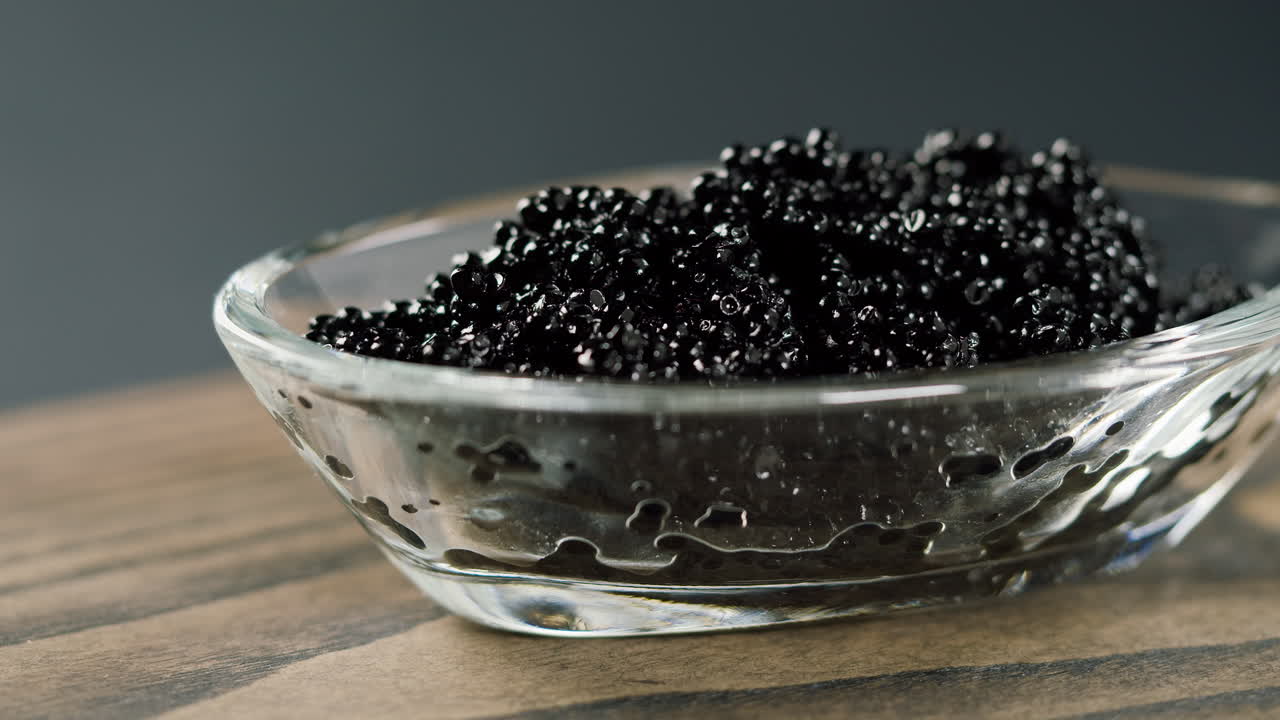 Prelevare caviale nero da una ciotola di vetro con un cucchiaio