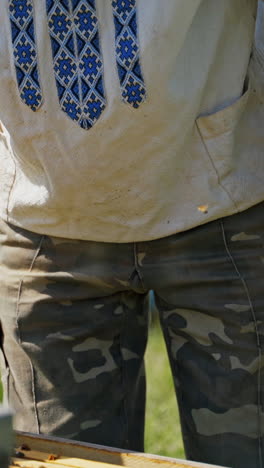 farmer in a bee-garden. beekeeper in a protective hat looking into beehives in an apiary in summer. beekeeping concept. vertical video