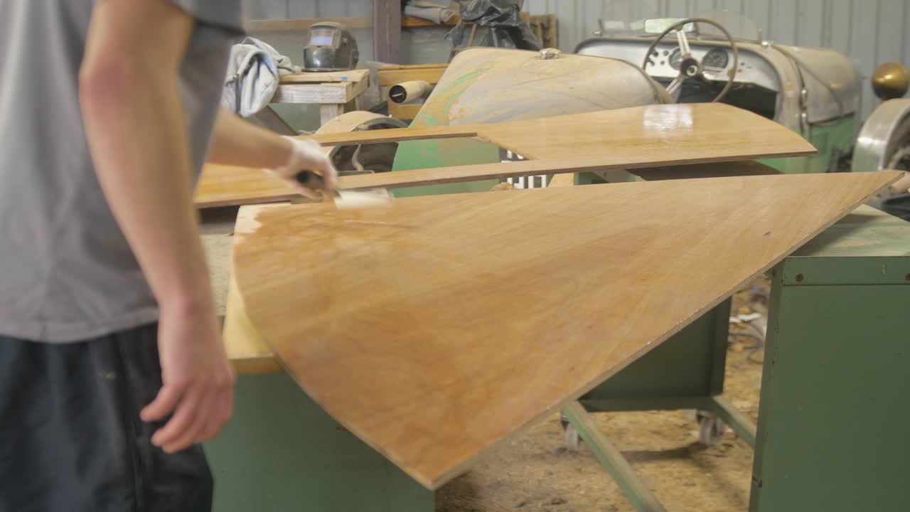 Man Applying Varnish to Plywood Boat or Car Parts in Workshop