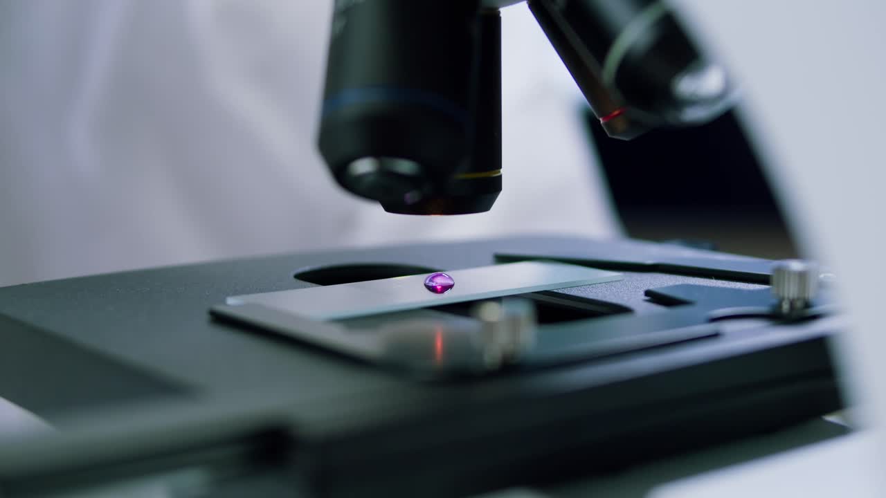 Scientist Adjusting Microscope Lens to Examine a Purple Sample