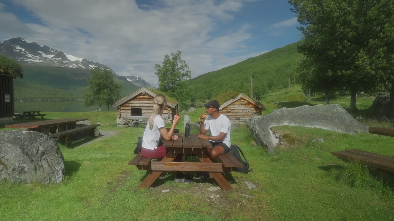 Couple Enjoying a Picnic and Apples in a Scenic Mountain Landscape with Traditional Cabins