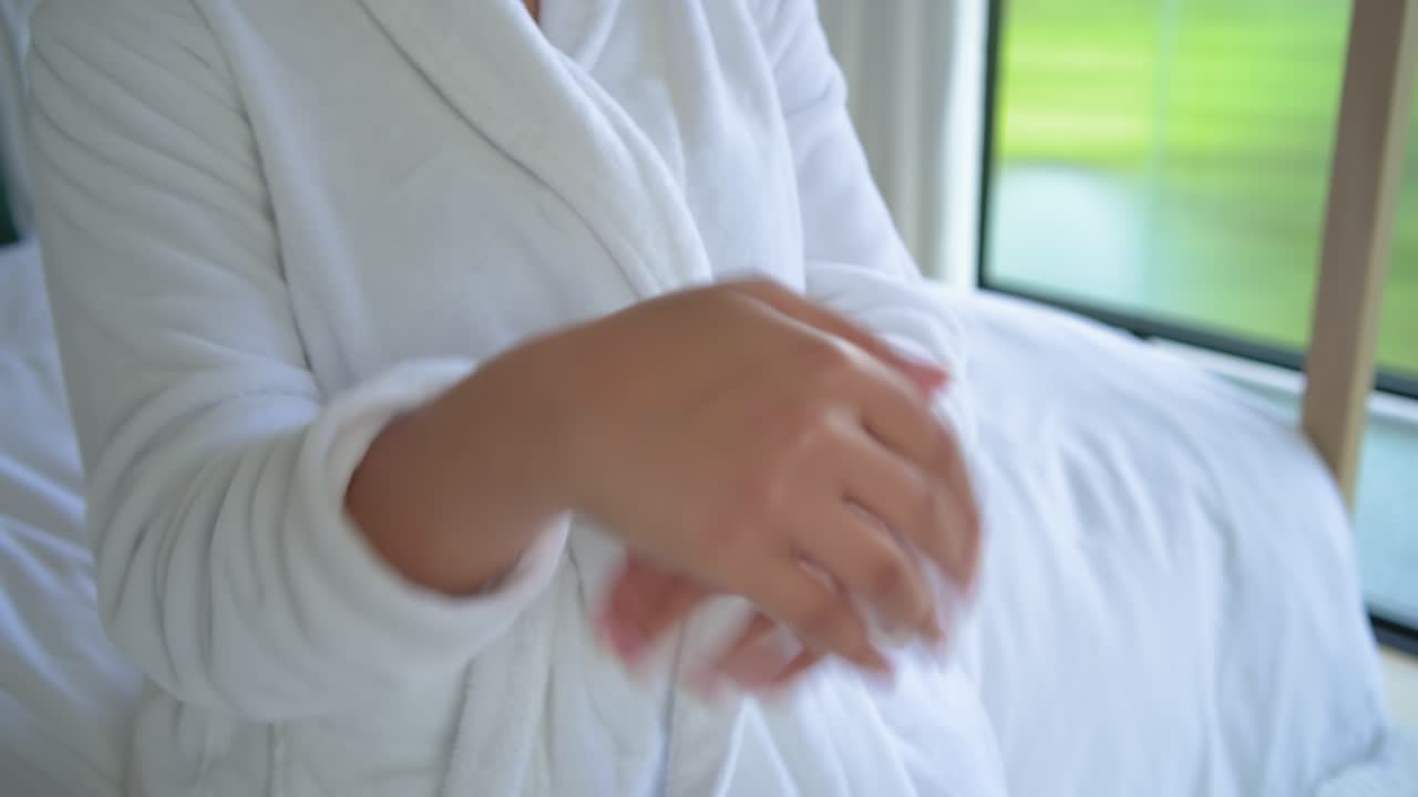 Mujer afroamericana extrayendo una pipeta de un frasco color ámbar, frotándose las manos con una bata junto a la ventana para su cuidado