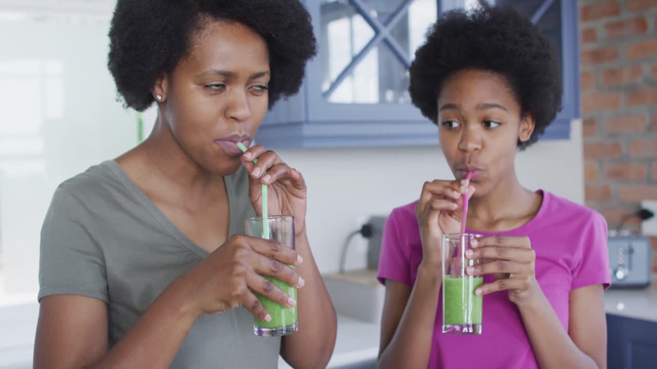 madre y hija afroamericanas felices bebiendo una bebida saludable en la cocina