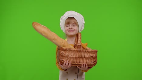 전문 요리사 요리사로 옷을 입은 소녀 아이가 미소 짓고 바게트와 을 가진 바구니를 보여줍니다.