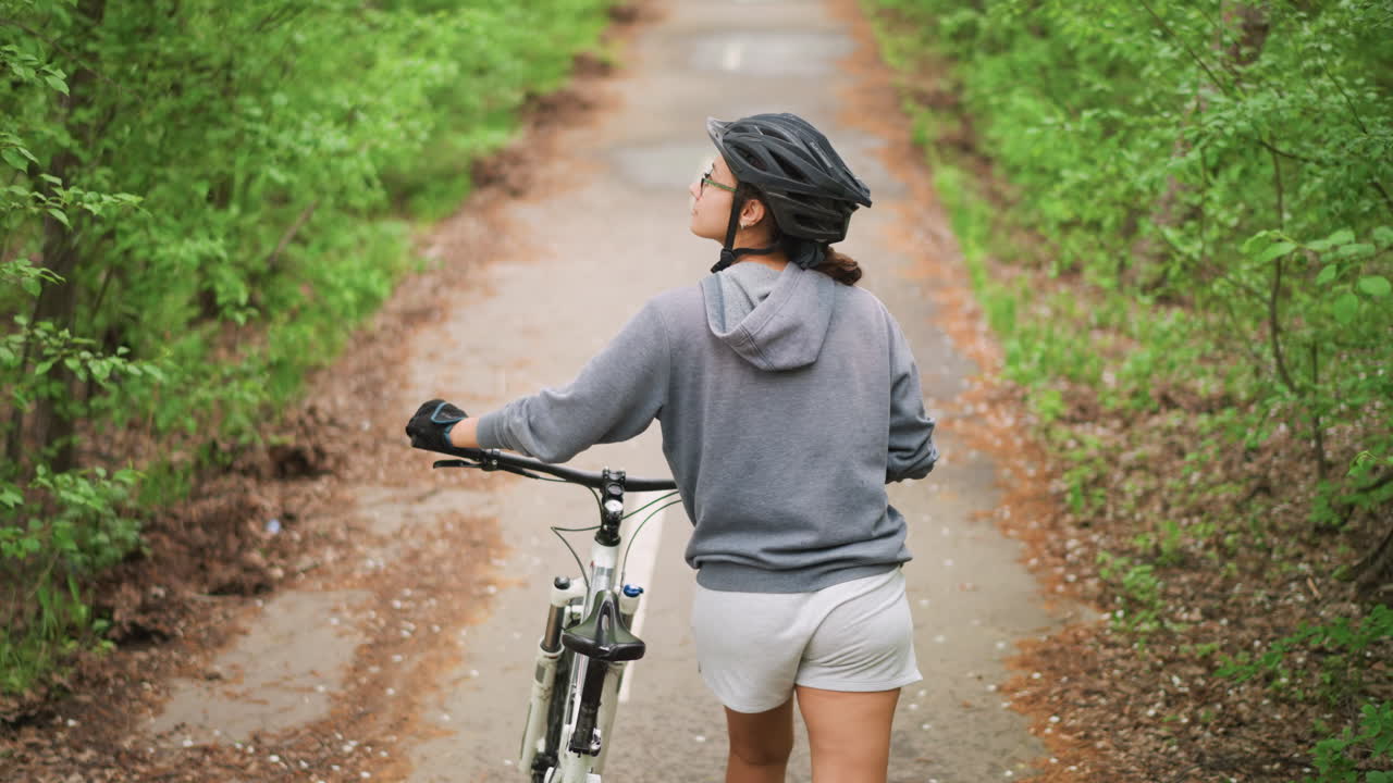 Pedestrian On Shaded Forest Path Pauses, Traveler On Leafy Trail Glances Back During Bicycle Stop, Individual Riding Bike Through Green Shade Briefly Halts To Observe Surroundings Distinctly