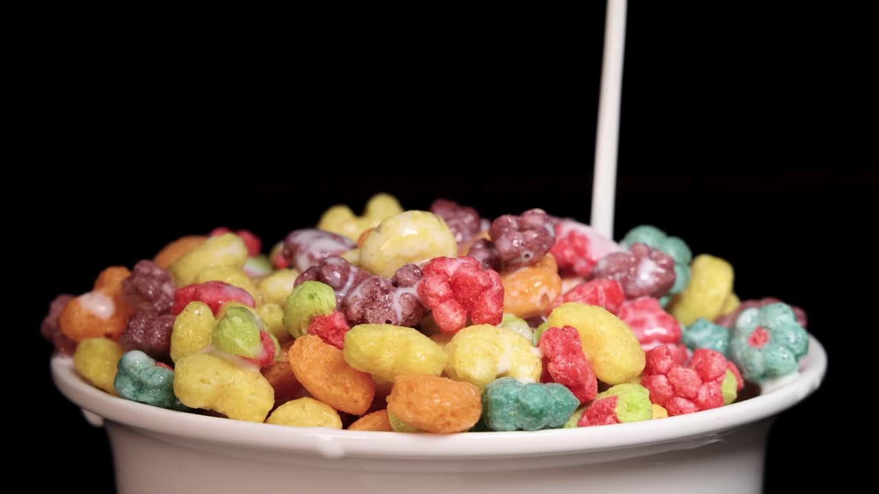 Milk cascades over vibrant cereal in slow motion, highlighting texture and color against a dark background