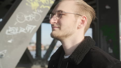 young european man with glasses, beard and man bun walking on sidewalk on a sunny evening in hamburg, germany