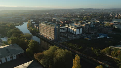 Establishing-Shot-of-Old-Industrial-Mill-turned-into-Apartments-in-Leeds-City-next-to-River-Aire-with-Reflections-at-Morning-Sunrise-West-Yorkshire-UK