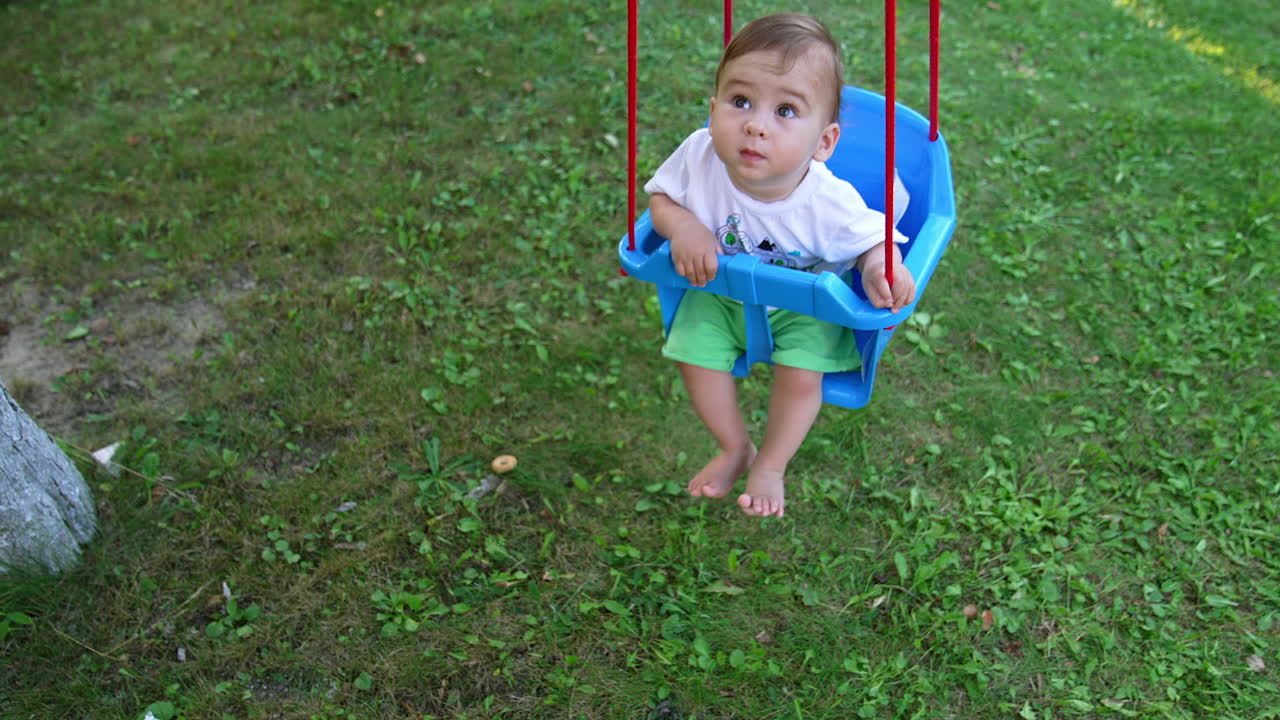 Small kid looking up while swaying on the swing. Adorable toddler boy spending time outdoors in the garden. View from top.