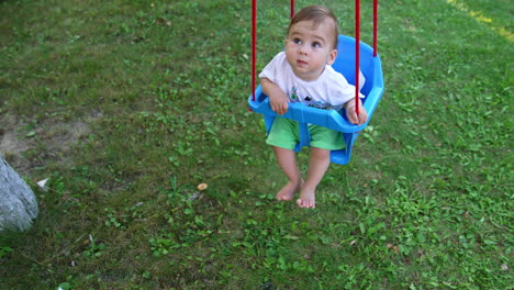 small kid looking up while swaying on the swing. adorable toddler boy spending time outdoors in the garden. view from top.
