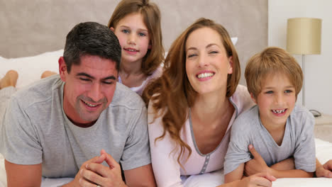 padres e hijos acostados en la cama sonriendo a la cámara