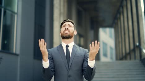 portrait young bearded businessman begs god for success with hope raising his hands up to sky