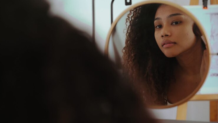 Young ethnic woman applying makeup near mirror