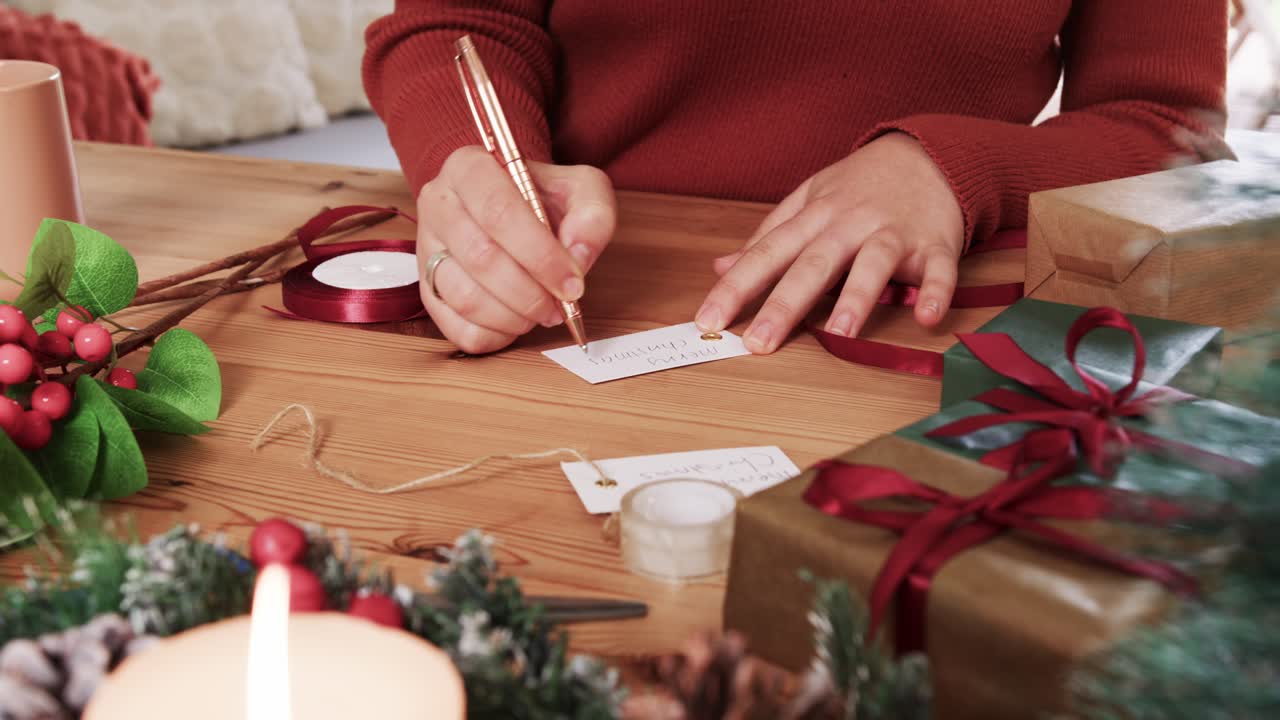 After placing blank tag on table, woman's hands are writing names to personalize holiday gifts