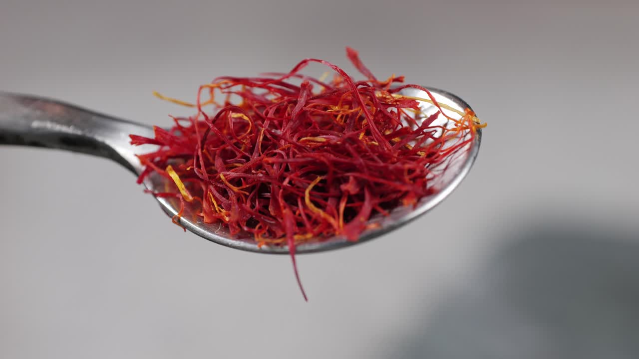 Dried crimson saffron on metall spoon close-up. Orange red spice for food. Crocus sativus flower saffron