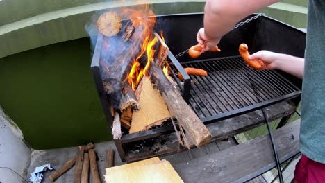 slow motion video of a white man putting sausages on a black grill with burning fire on a sunny day