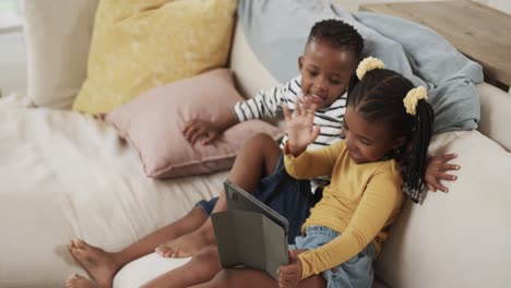 Happy-african-american-brother-and-sister-using-tablet-relaxing-on-sofa-at-home,-slow-motion