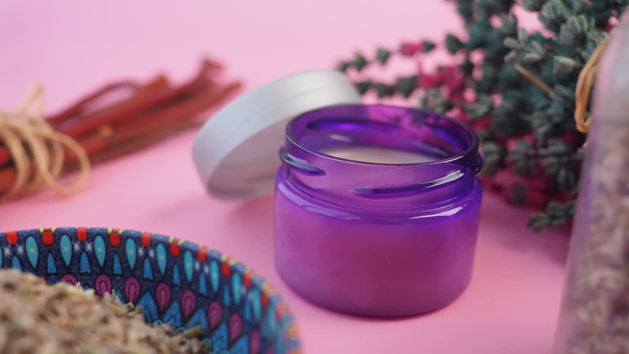 Lilla krukke med naturlig creme med lavendel og urter på lyserød baggrund.