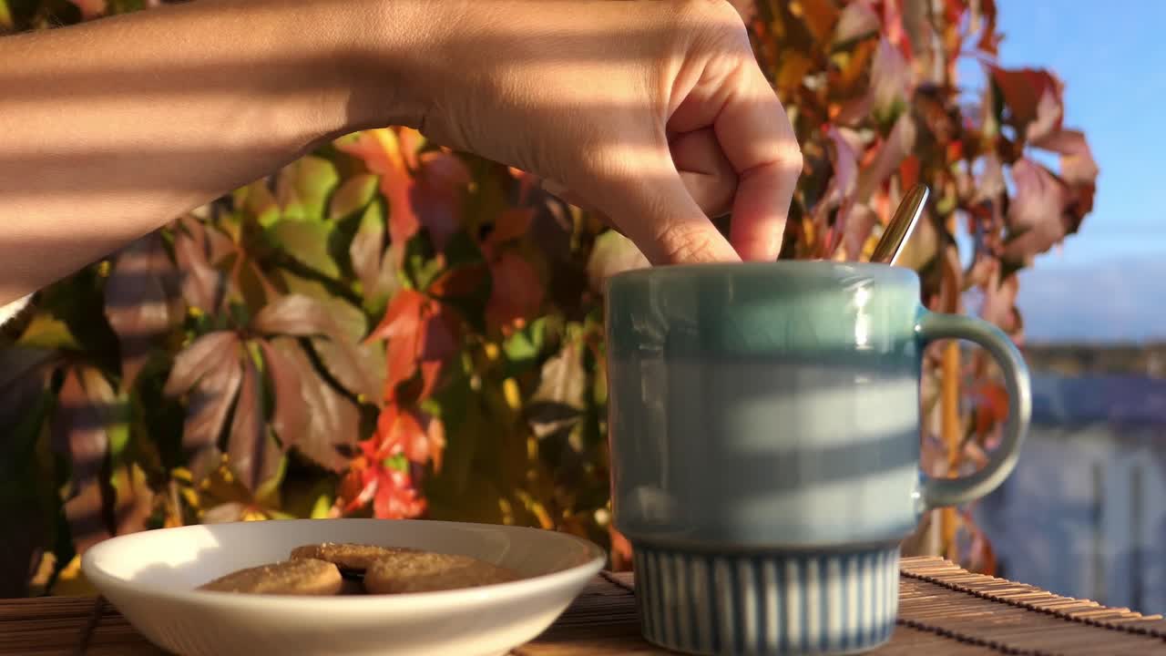 mujer sumergiendo galletas en una bebida caliente con coloridas hojas de otoño en el fondo