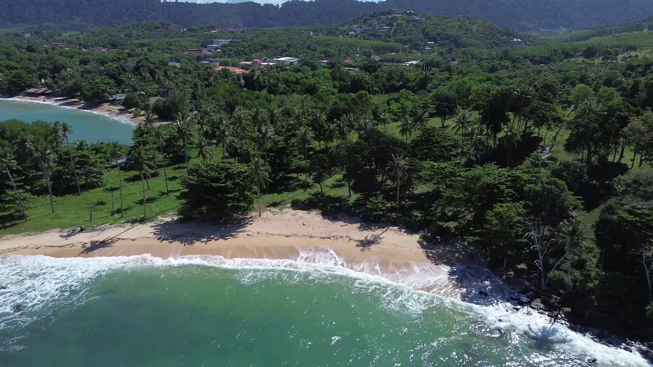 Aerial drone footage flying above palm trees revealing a hidden tropical beach with turquoise ocean on Koh Lanta island in Thailand, showing scenic untouched coastline and exotic paradise landscape