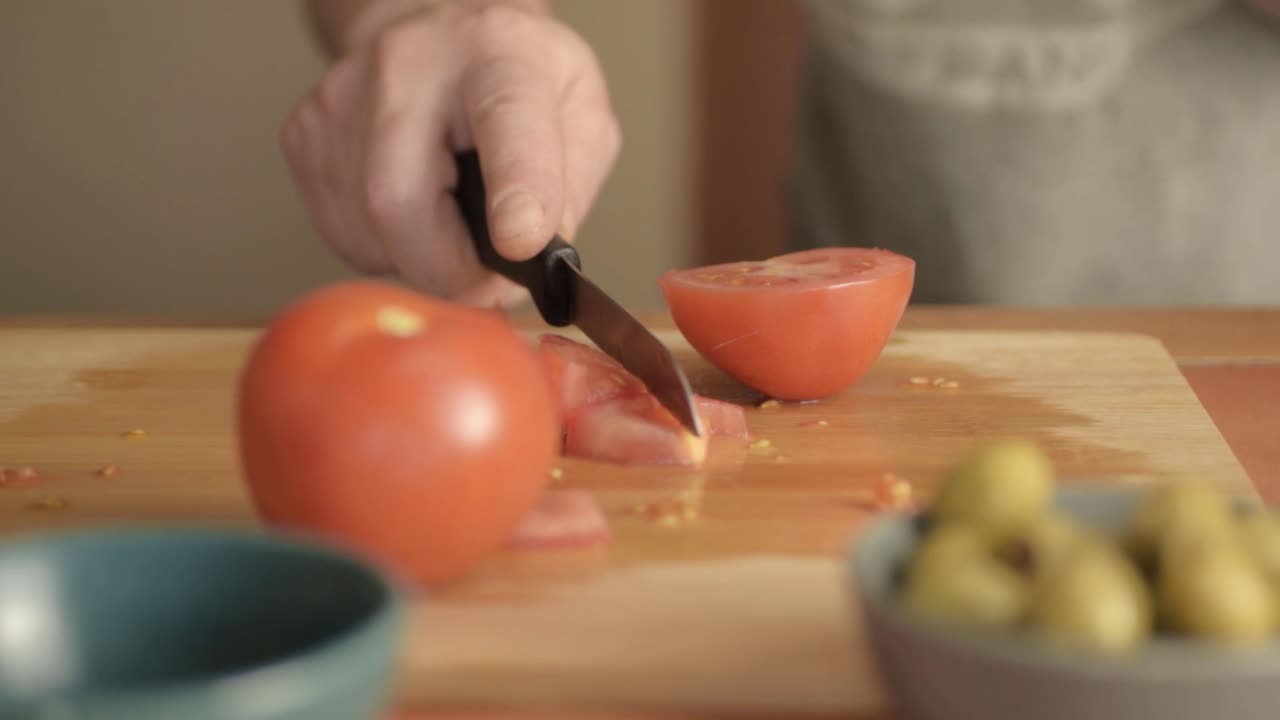 manos cortando tomates frescos en rama en una tabla de cortar con aceitunas primer plano