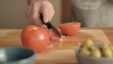 Hands-chopping-fresh-vine-tomatoes-on-chopping-board-with-olives-close-up-shot