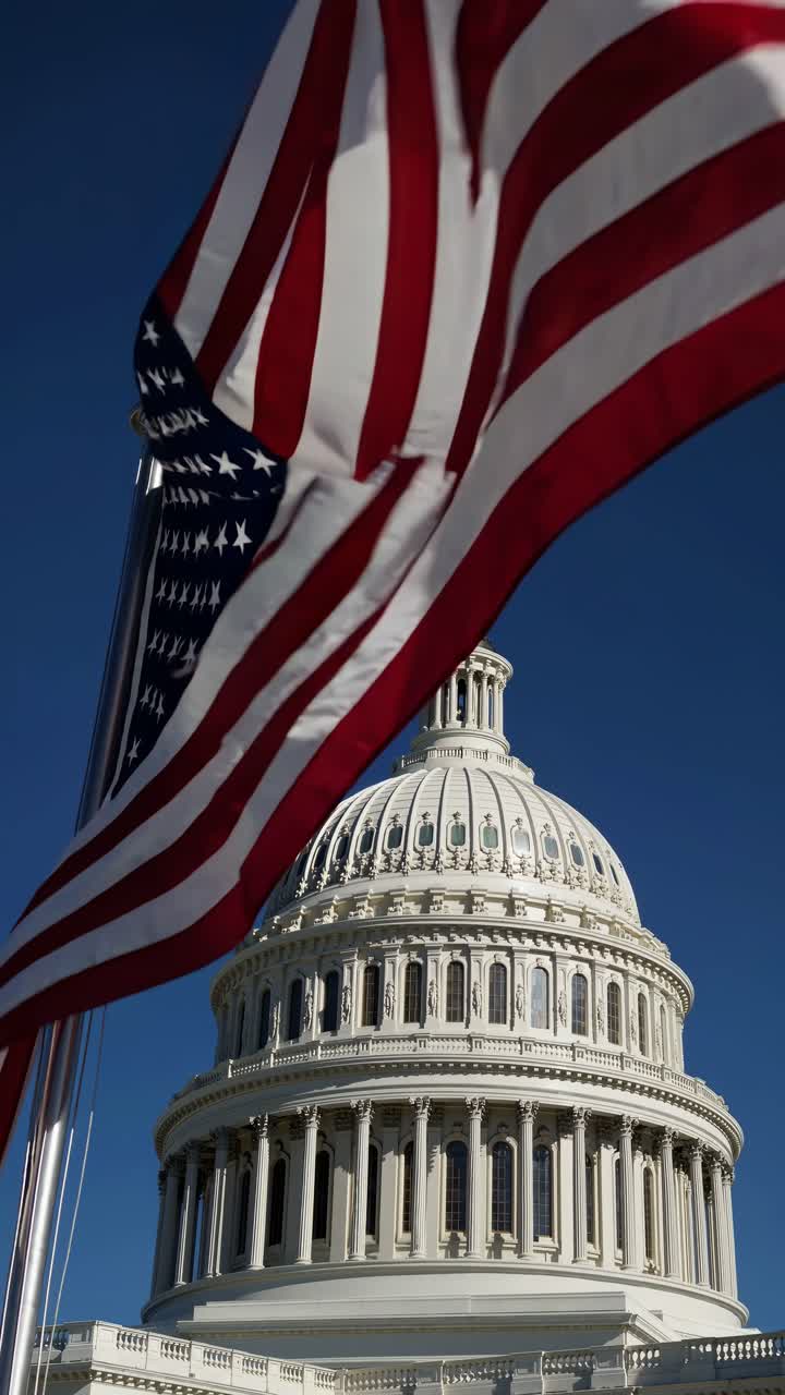 Low-angle video shot of the U.S. Capitol dome with a waving American flag in the foreground