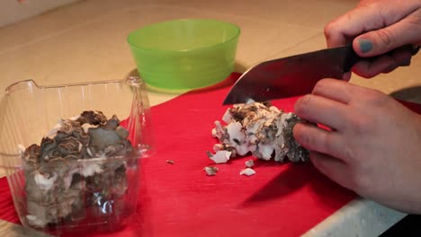 Manos-Cortando-Un-Racimo-De-Champiñones-Maitake-En-Una-Tabla-De-Cortar-Roja-Con-Un-Cuchillo-De-Chef-Santoku-Y-Poniendo-Champiñones-Cortados-En-Un-Bol