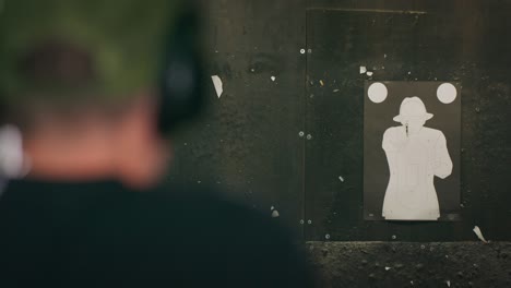 rear view of a defocused man wearing ear protection aiming a pistol and shooting at a target at an indoor firing range
