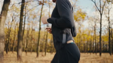 side view close up of a man in a black sports uniform running along the earth path in the morning sunny autumn forest