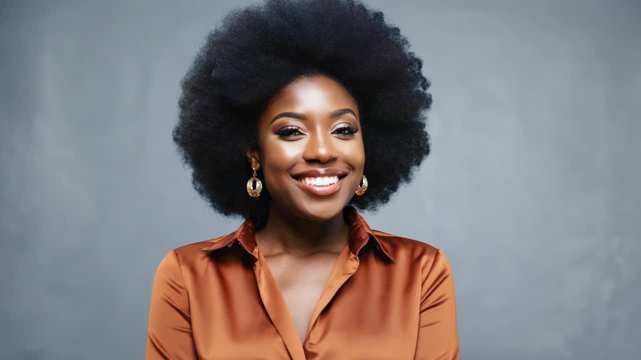 Professional headshot featuring confident black woman with natural afro hairstyle, wearing brown top, smiling warmly toward viewer on neutral gray backdrop