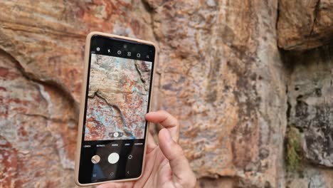 Close-up-of-a-hand-of-a-person-taking-a-picture-with-a-cell-phone-of-some-cave-paintings-in-a-mountain-shelter