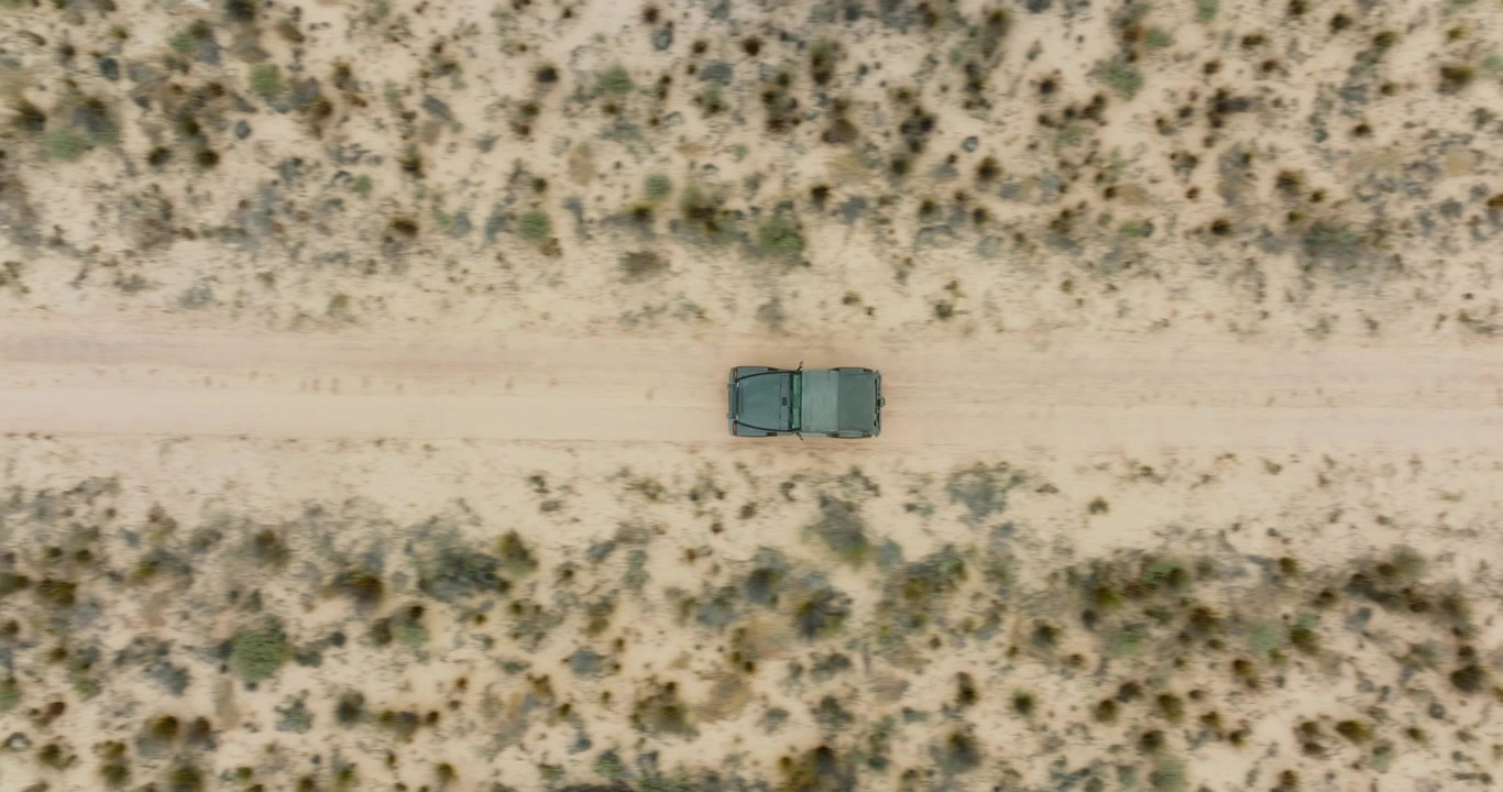 Drone che vola con vista a volo d'uccello su un paesaggio desertico nell'area selvaggia di Cederberg in Sudafrica, sopra una strada nel deserto dove sta guidando un veicolo fuoristrada nero