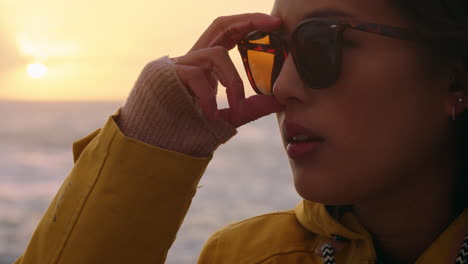 portrait of happy asian woman wearing sunglasses enjoying vacation exploring travel lifestyle relaxing on beach feeling positive at sunset