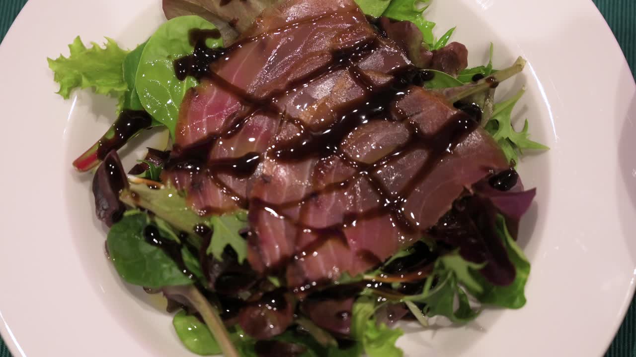 A dish of sliced smoked tuna and salad, topped with sweetened vinegar is seen on a plate