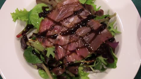 a dish of sliced smoked tuna and salad, topped with sweetened vinegar is seen on a plate