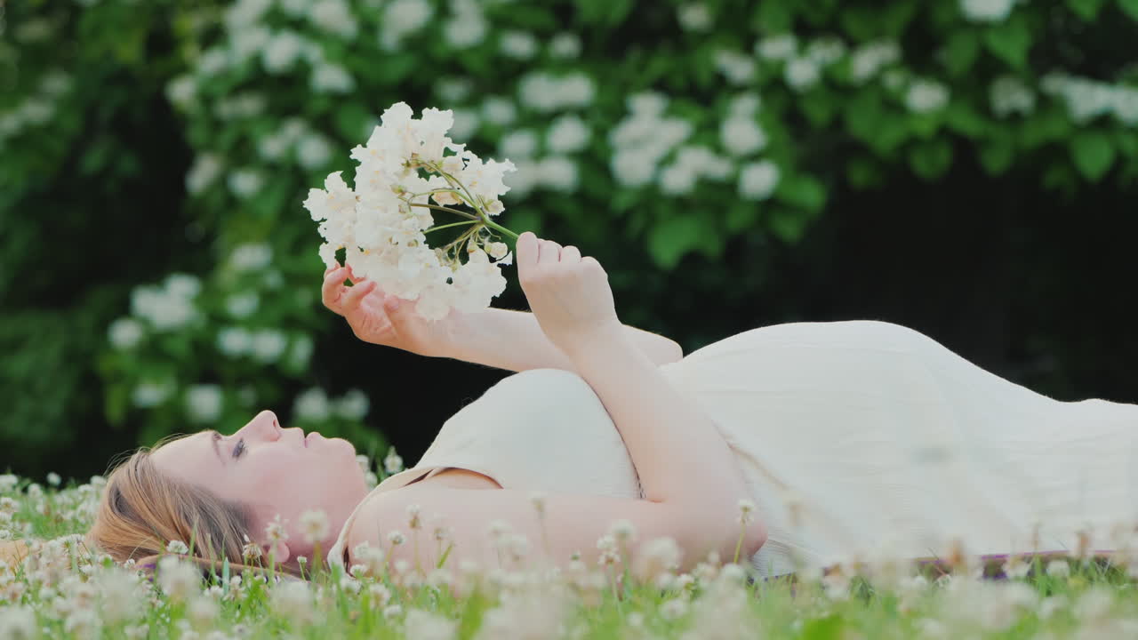 꽃을 들고 잔디밭에 누워 매력적인 임신한 여자