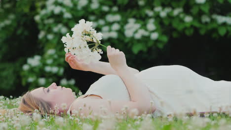 Attractive-Pregnant-Woman-Lying-On-The-Lawn-Holding-A-Flower